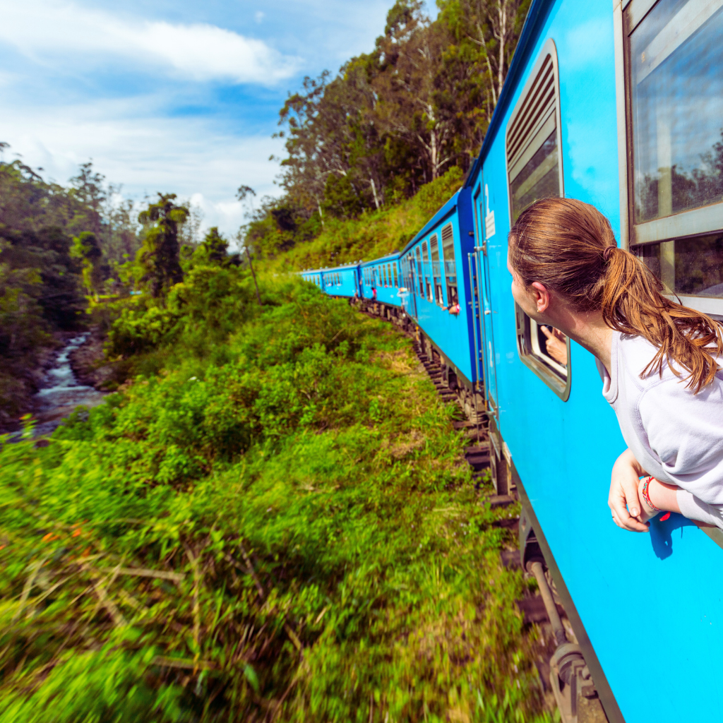 Traveler enjoying scenic views from a blue train on Sri Lanka's famous hill country route